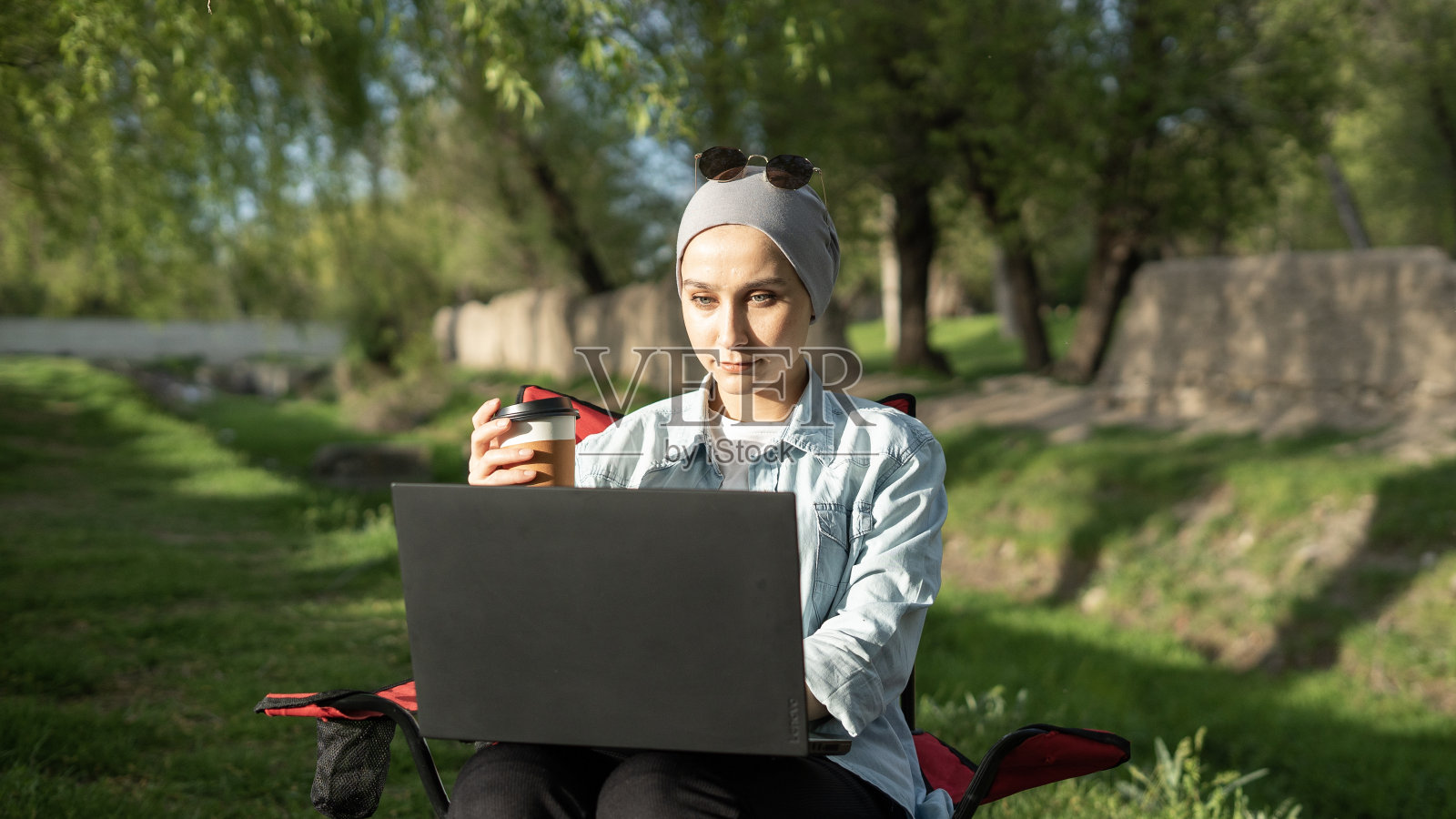 戴头巾的年轻女子在自然公园边喝咖啡边用笔记本电脑工作照片摄影图片