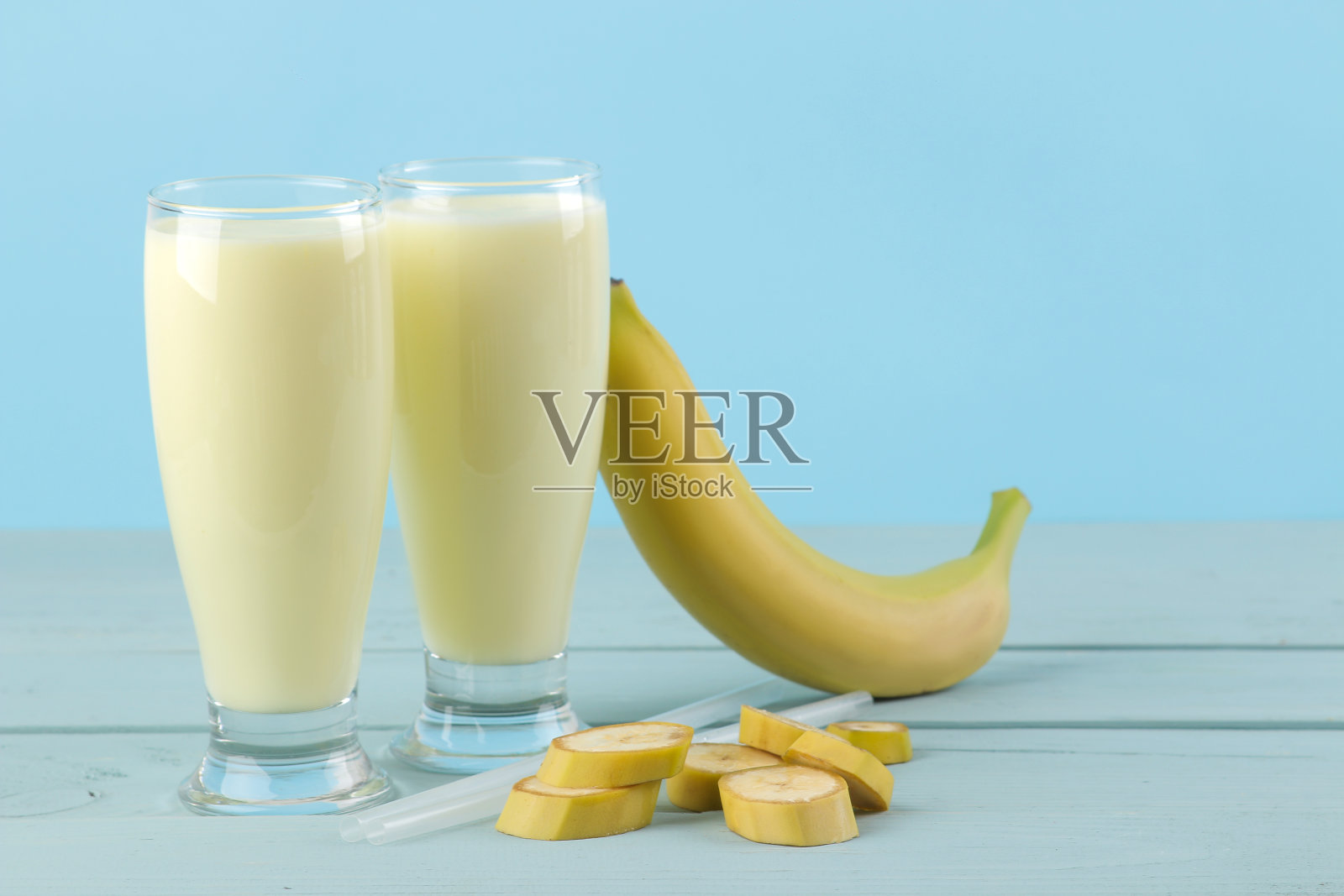 一杯香蕉奶昔和一根蓝色背景的新鲜香蕉。做奶昔。照片摄影图片