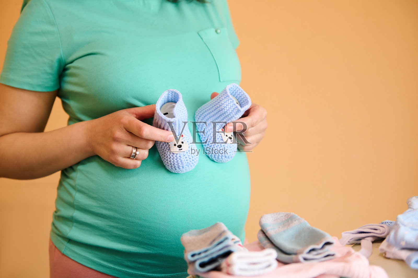 孕妇在为妇产医院折叠东西时，将可爱的婴儿靴套在肚子上。照片摄影图片