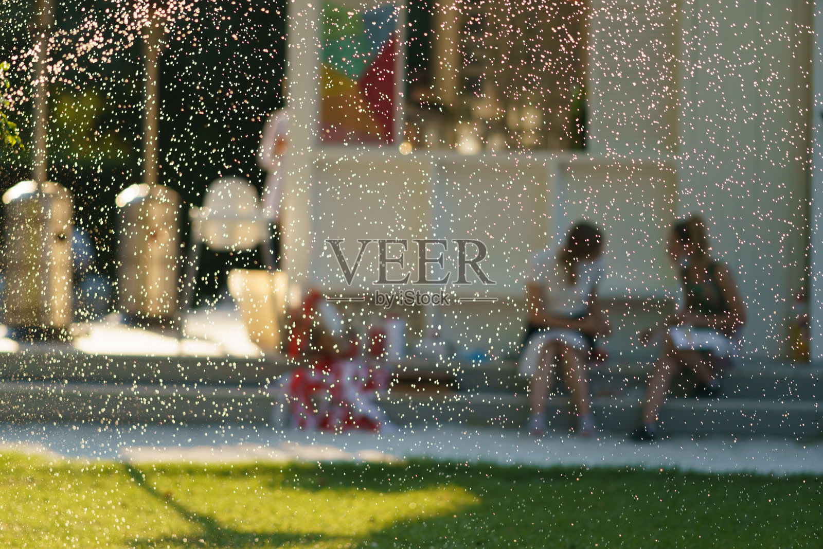 年轻女子在莫斯科公园的喷泉前休息。他们说话。在一起很开心。前景中喷泉的水滴。关注前景。模糊的背景。幸福照片摄影图片