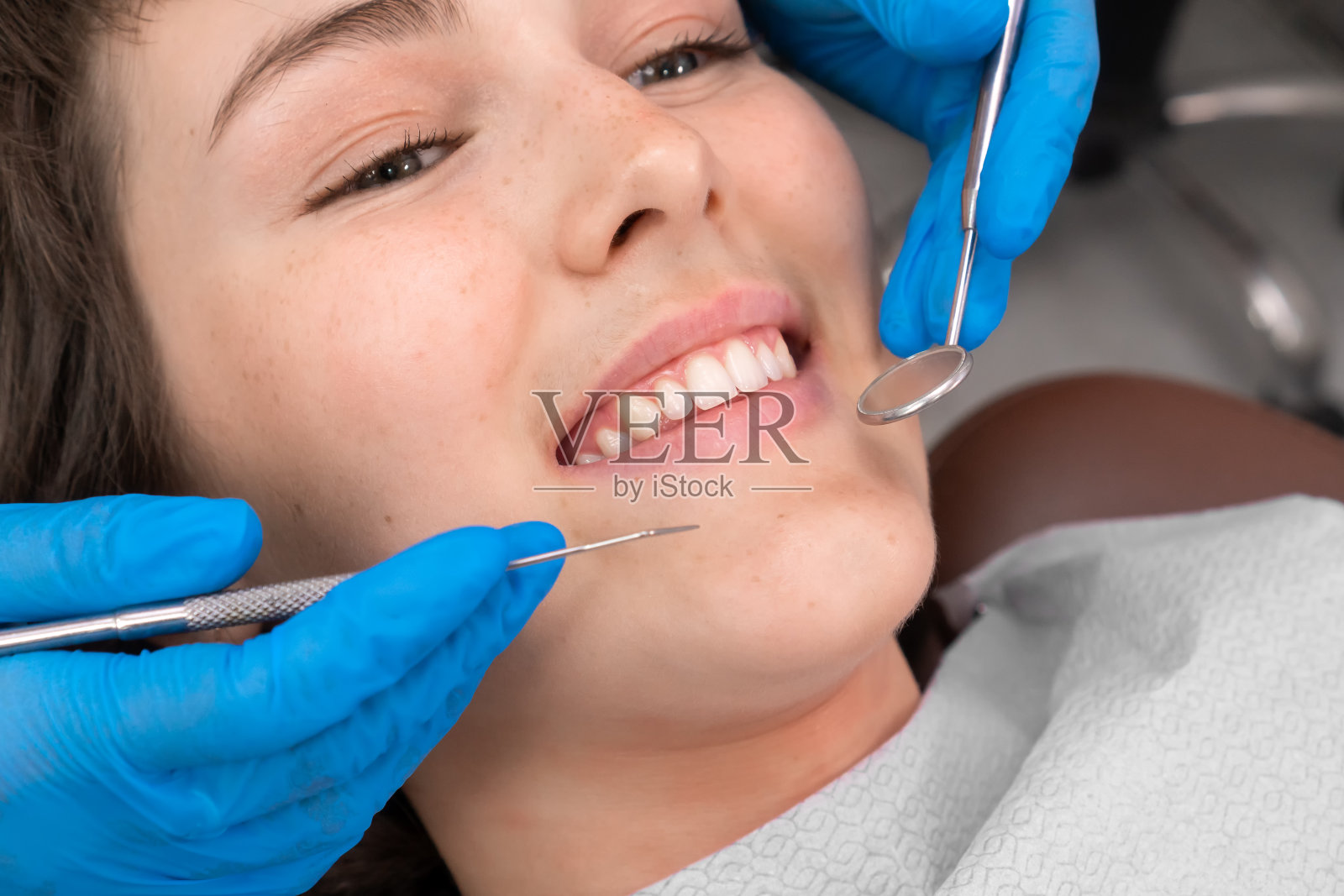 开朗的女士露出洁白的牙齿微笑，牙医用双手将牙科器械送到她的嘴里照片摄影图片