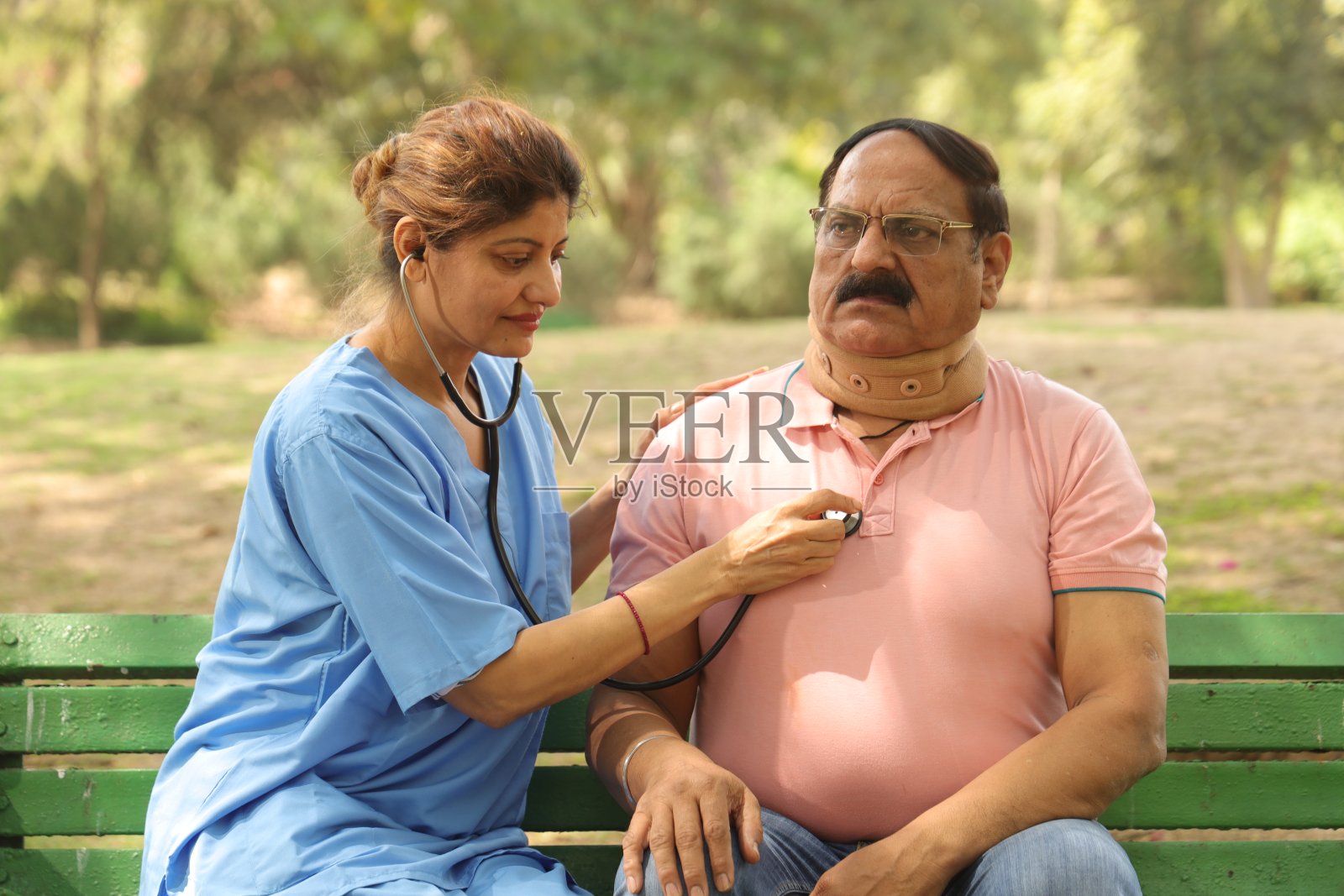 快乐的印度女医生正在给一位中年男子做检查，两人都坐在公园的长椅上。照片摄影图片