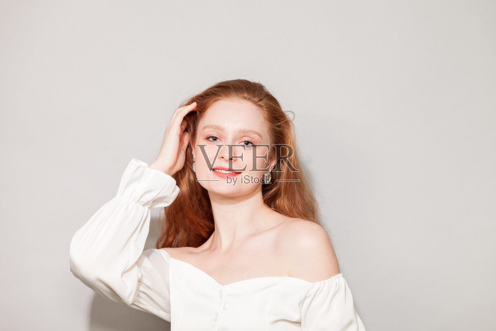 画室里一位年轻迷人、开朗的红发女子的肖像，她身穿白色衬衫，背景是灰色的照片摄影图片