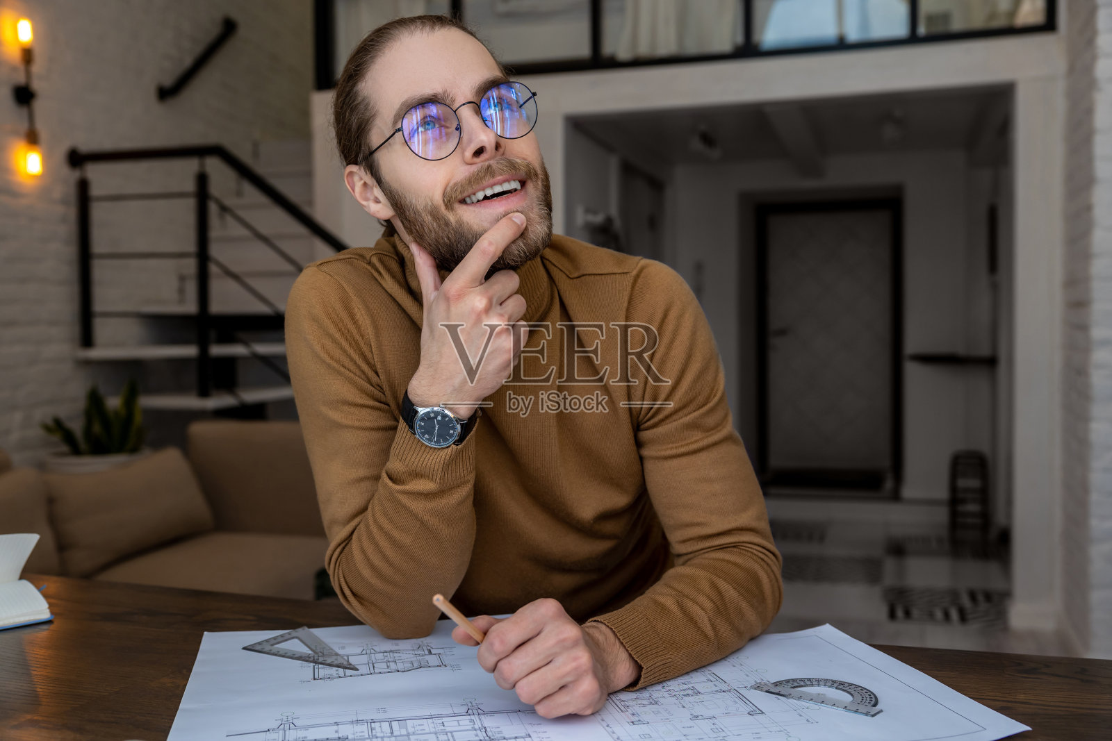 戴着眼镜的工程师建筑师坐在桌子旁，创造蓝图，思考新项目照片摄影图片