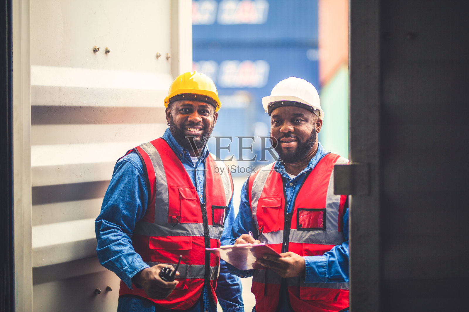 Portrait of Two African Engineer or foreman wears PPE checking container storage with cargo container background at sunset. Logistics global import or export shipping industrial concept.照片摄影图片