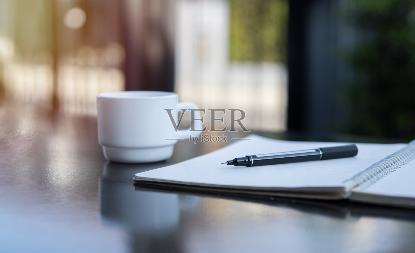 Side view image of an open notebook, pen and cup of tea on the black table at outdoor.照片摄影图片