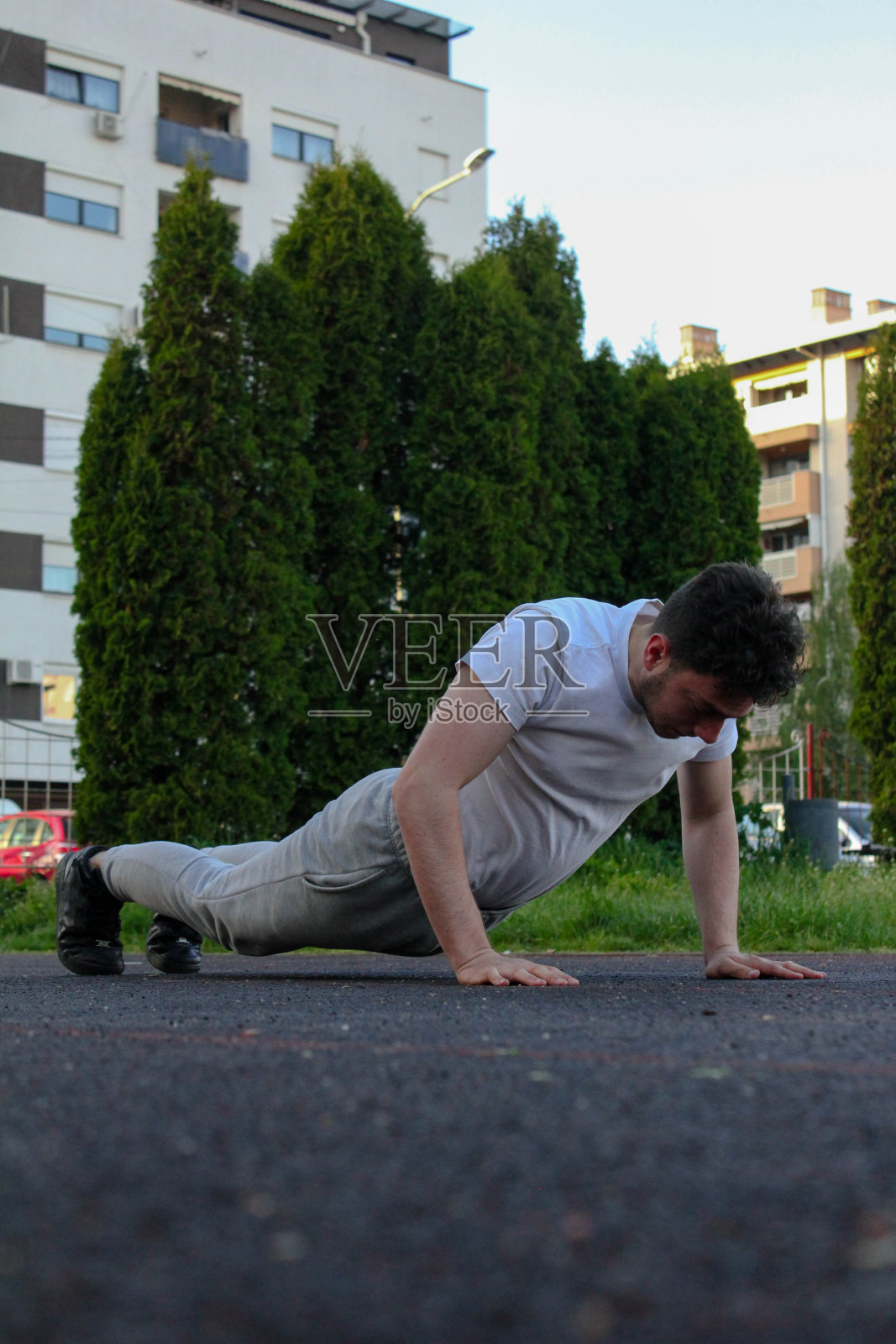 A white man jumping from the ground while doing a pushup in a public park照片摄影图片