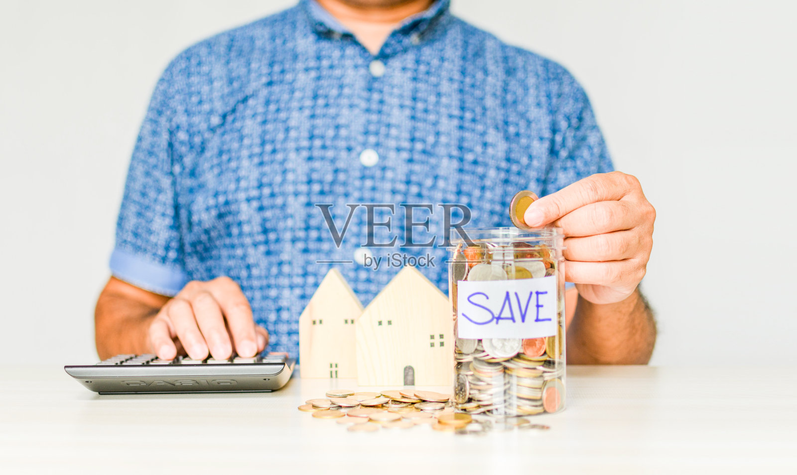 特写，男子坐在一个罐子里，拿着并收集一枚硬币。在COVID或冠状病毒爆发期间，男性收集房屋和汽车付款的概念。右拷贝空间。模糊的白色背景照片摄影图片