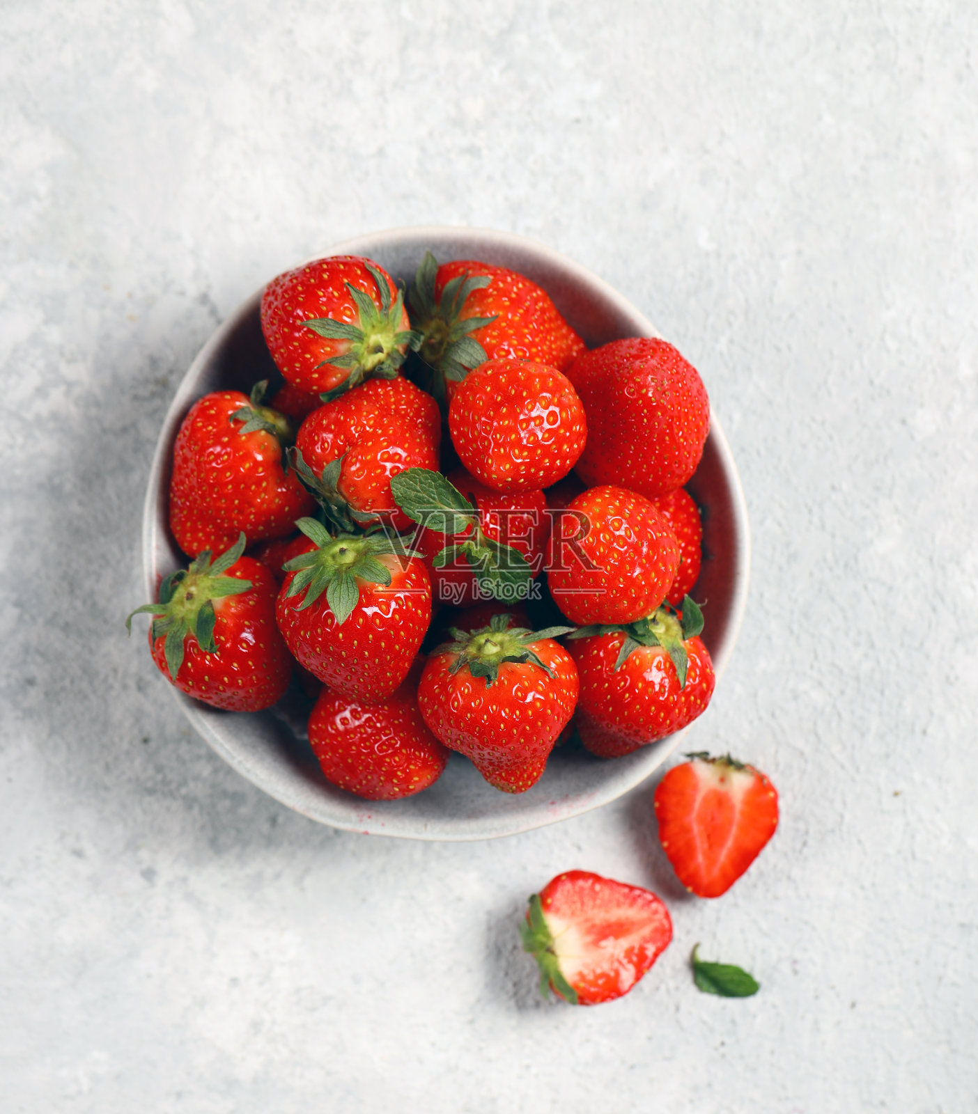 浅灰色背景上，一个灰色盘子里放着新鲜成熟的草莓照片摄影图片