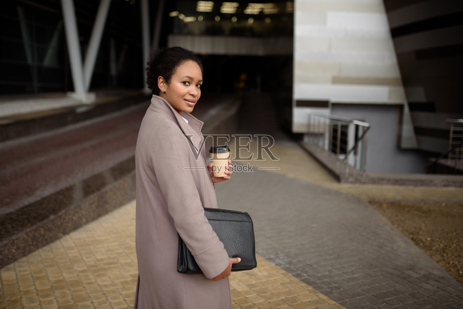 微笑的非裔美国妇女拿着文件夹和咖啡在办公楼附近照片摄影图片