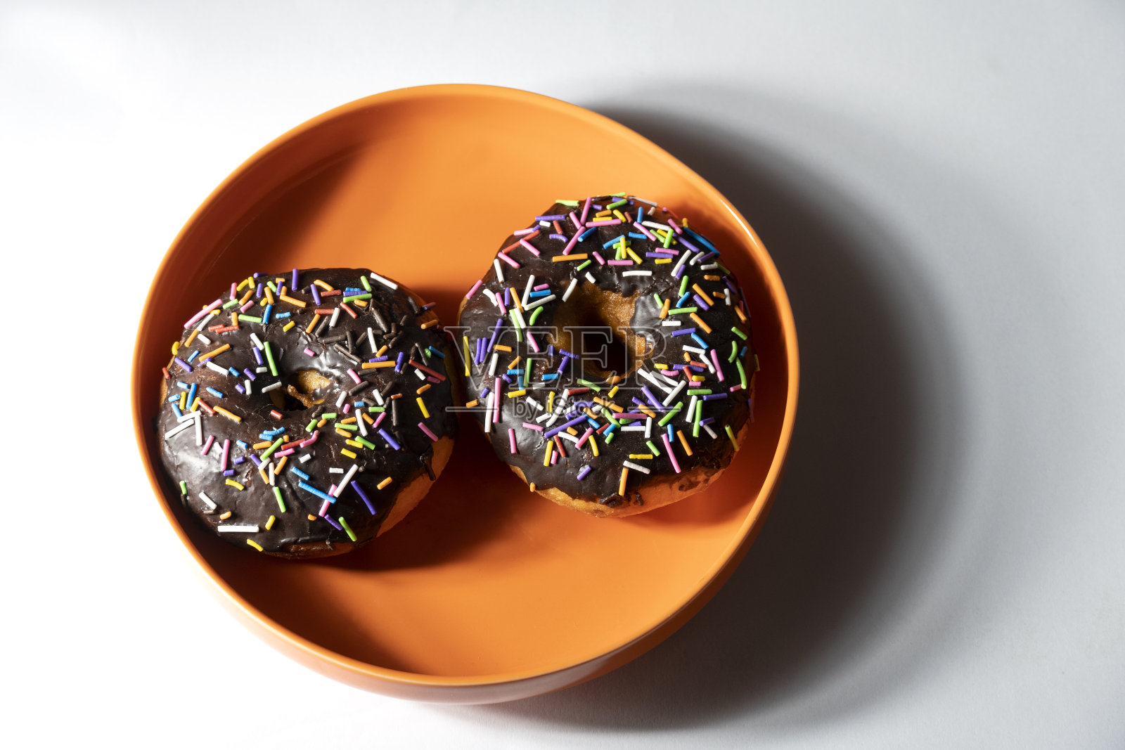 彩色的甜甜圈在白色背景上的橙色盘子上。俯视图照片摄影图片