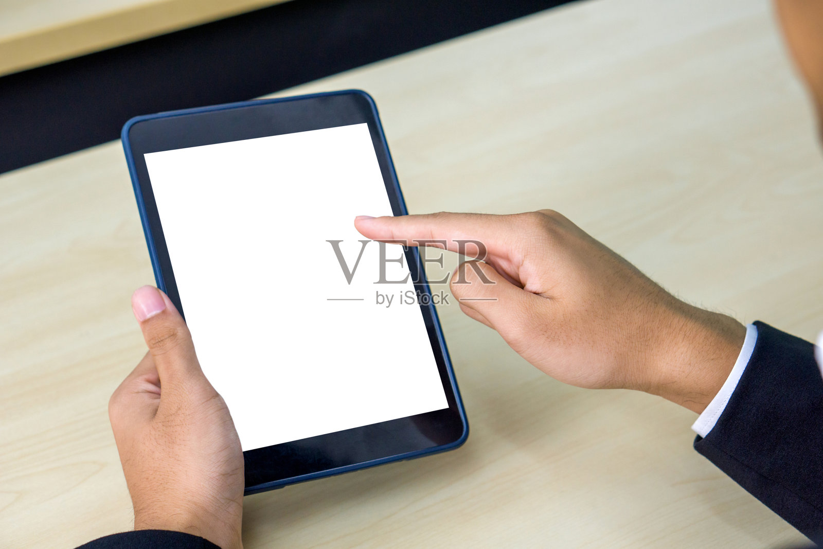 一位身穿黑色西装的商人坐在木桌旁，手指着空白的屏幕。照片摄影图片