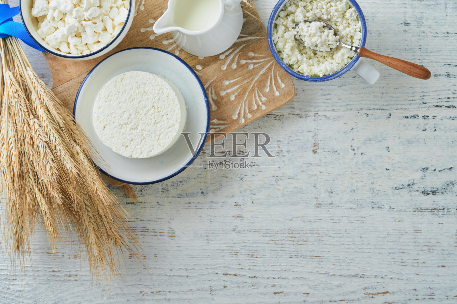 犹太节日Shavuot庆典。洁食新鲜乳制品牛奶和奶酪，成熟的小麦，奶油在白色木制背景。白色木制背景上的乳制品。Shavuot概念。前视图。照片摄影图片