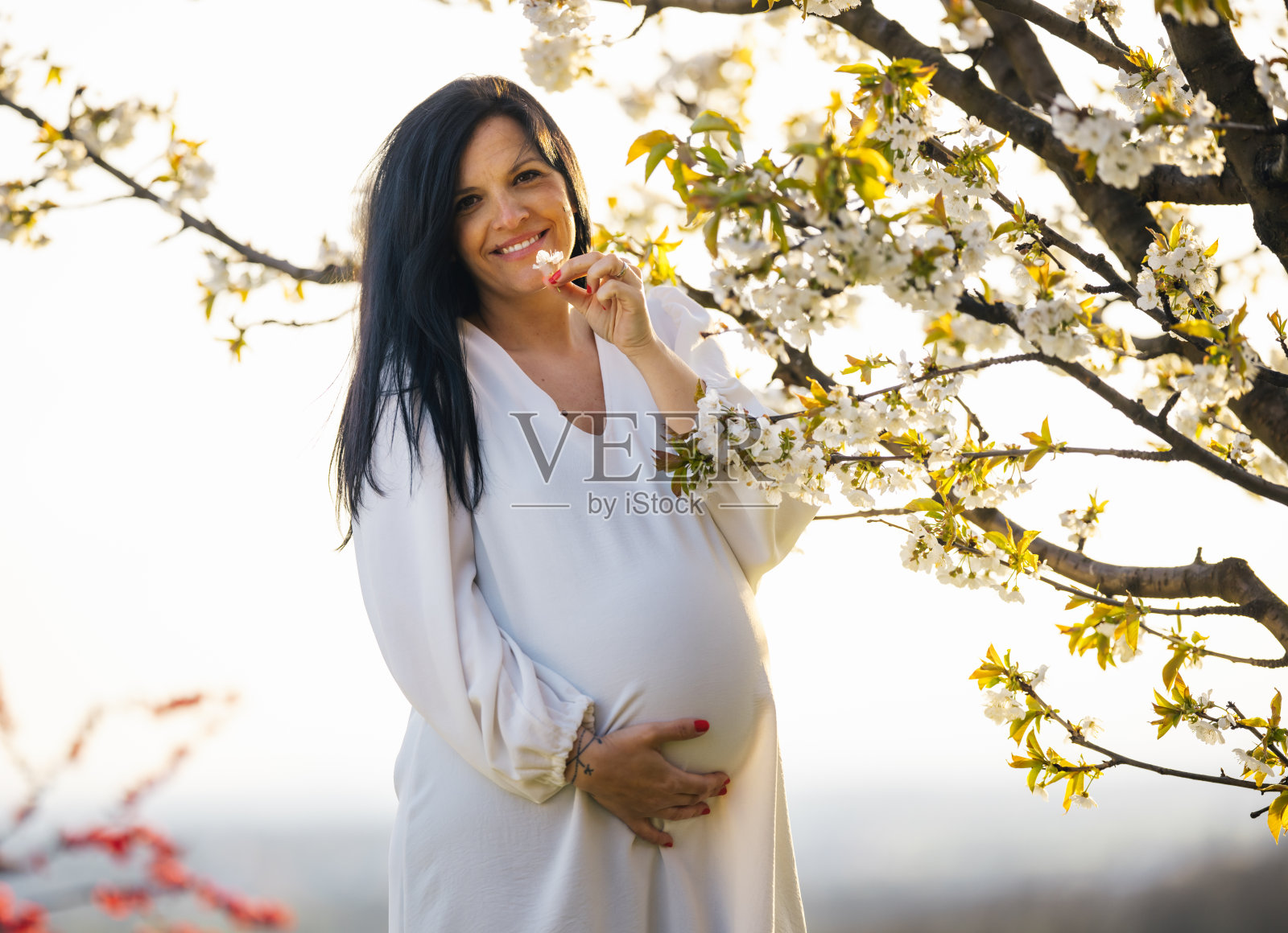 一位美丽的年轻孕妇在户外放松，闻着樱桃树的花香。快乐的孕妇在大自然中享受轻松的产假照片摄影图片