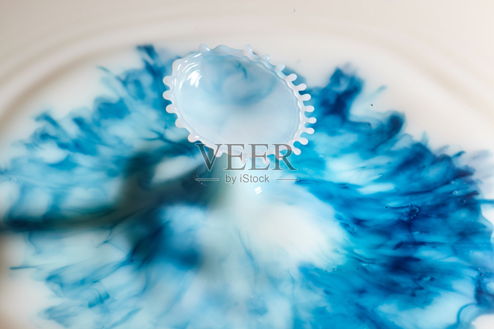 乳白色的水滴，带有蓝色墨水的细卷须，从液体表面展开照片摄影图片