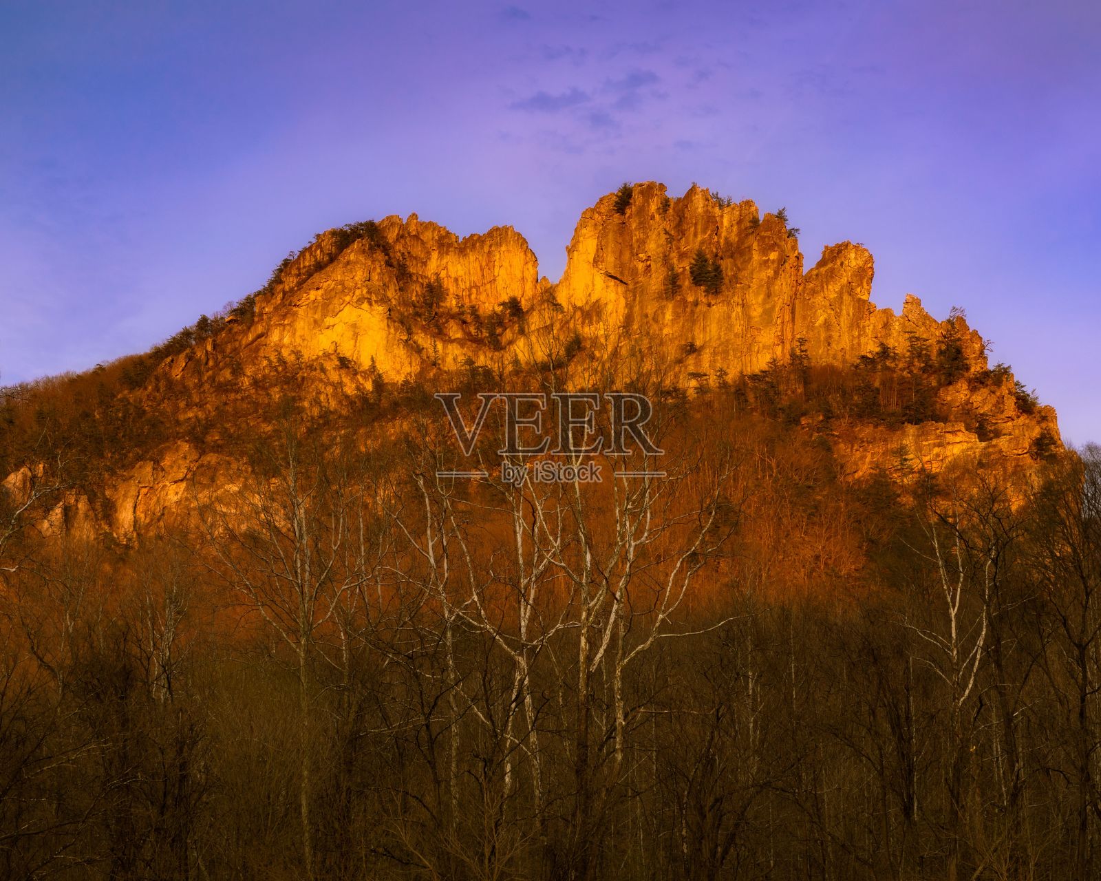 一座山，太阳落在前面的树木和灌木丛后面照片摄影图片