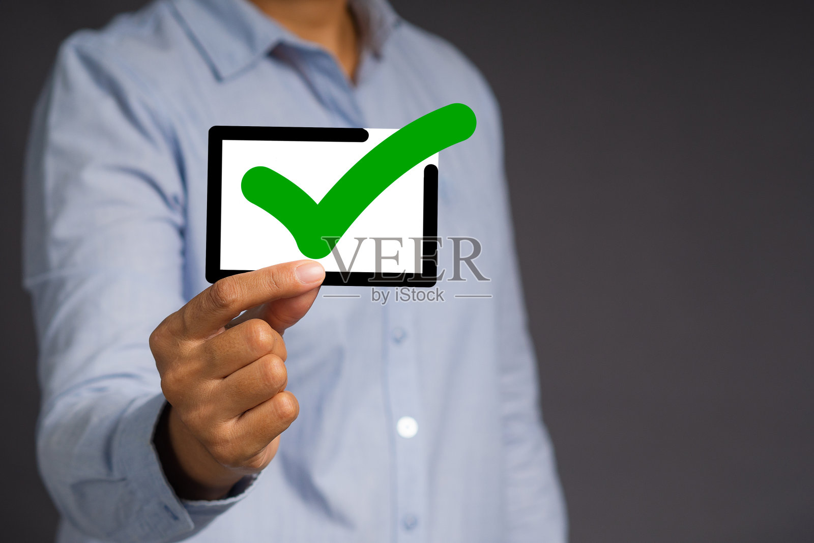 手拿着黑色边框的绿色勾号符号，站在灰色背景下。照片摄影图片