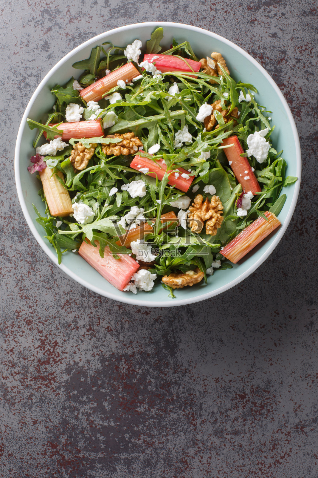 沙拉与烤大黄，芝麻菜，山羊奶酪和核桃与蜂蜜酱近在一个碗。垂直俯视图照片摄影图片