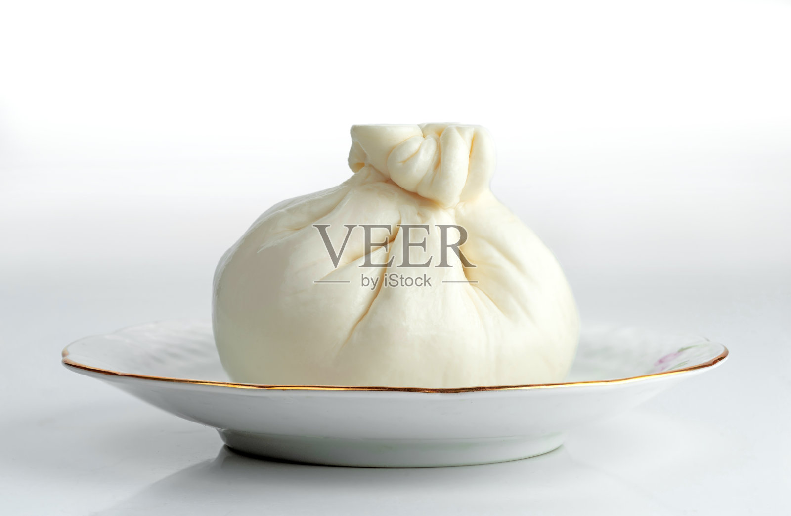 一颗典型的意大利牛奶布拉塔奶酪放在瓷碟上。照片摄影图片