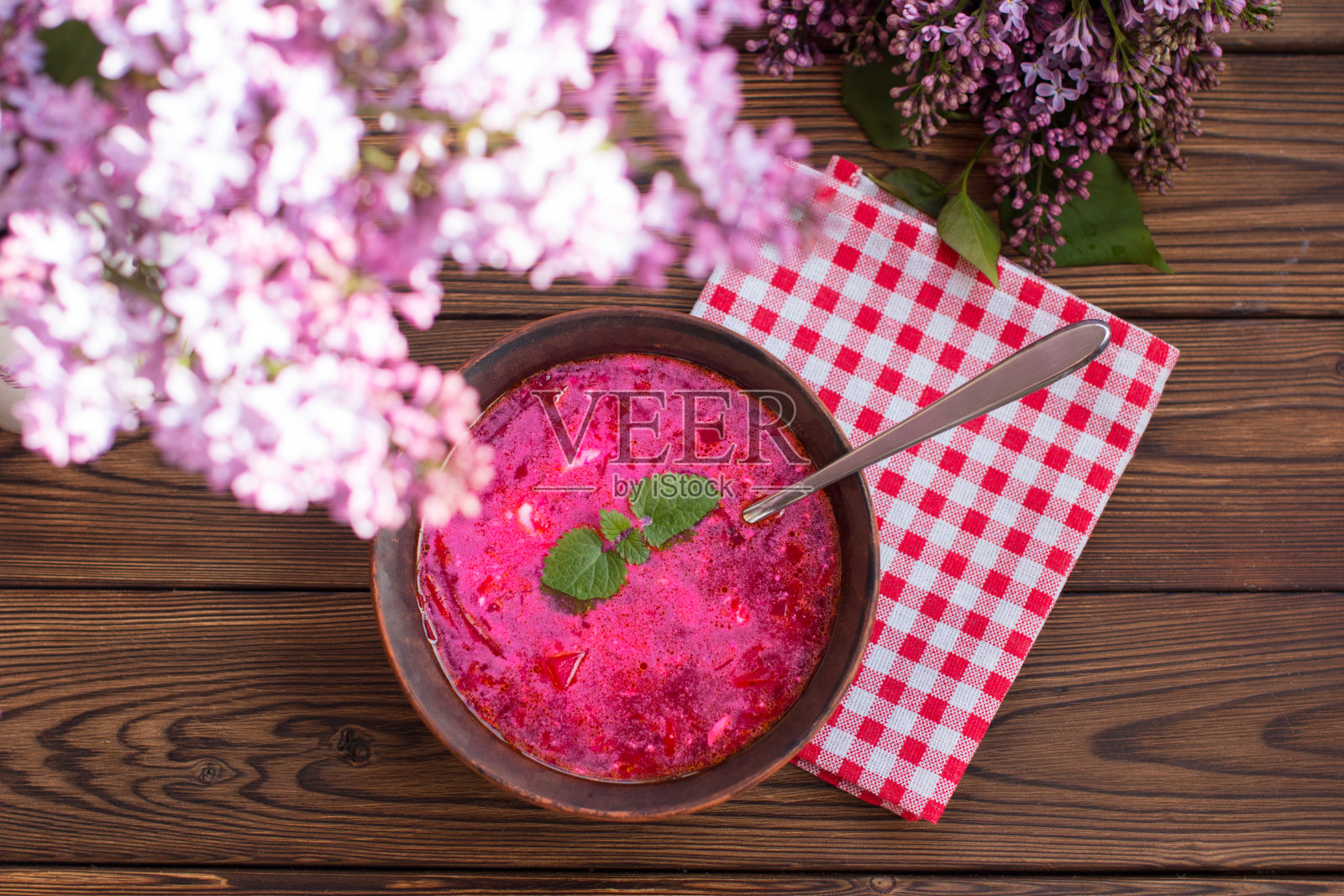 新鲜的红罗宋汤配酸奶油和甜菜根，放在木制背景的陶瓷盘子里。丁香花香，乡村风格照片摄影图片