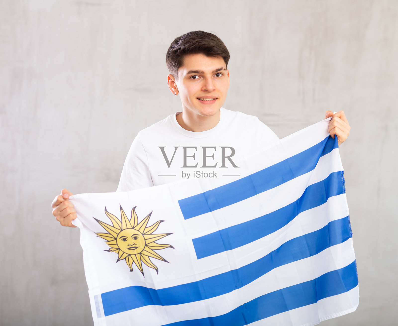 快乐的年轻人手持乌拉圭国旗，背景是单色的照片摄影图片