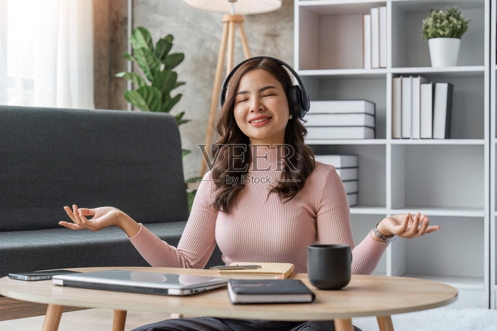 听音乐的女人，戴着耳机，坐在客厅的沙发上，快乐的年轻女士闭着眼睛享受音乐照片摄影图片