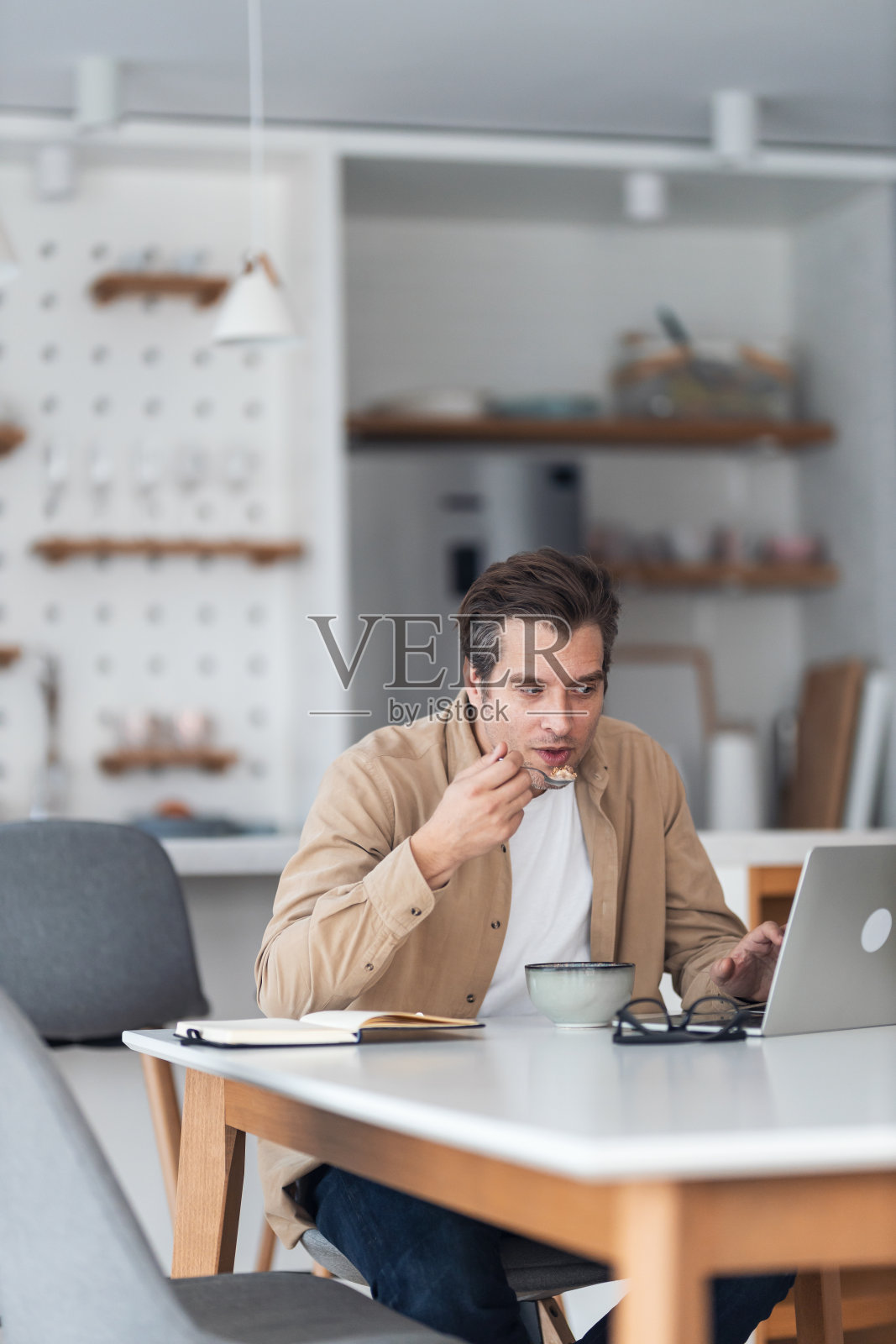 一个严肃的男性自由职业者在家里用笔记本电脑工作，吃着麦片配牛奶。照片摄影图片