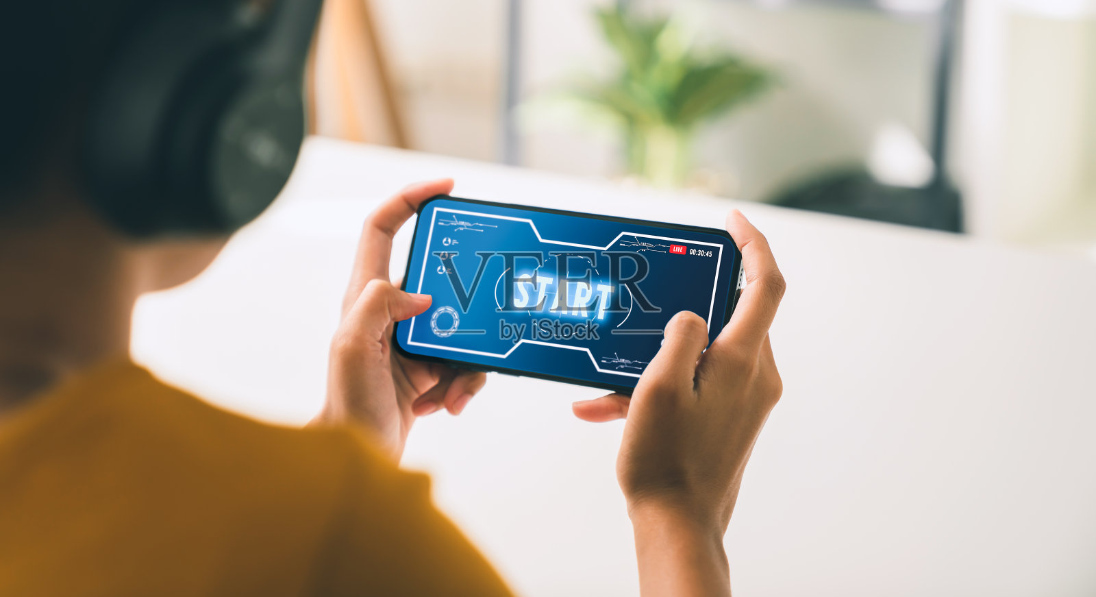 兴奋的年轻女子戴着耳机，在智能手机上玩网络游戏，在互联网上直播。照片摄影图片