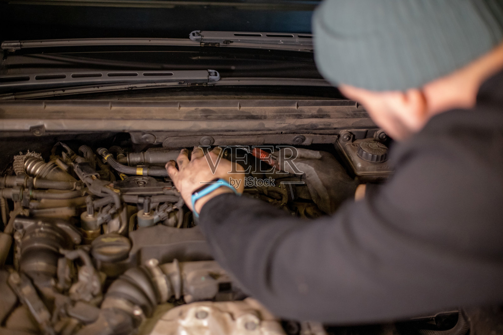 一个年轻人独自在家修车。他戴着手套，使用手工工具。他的手和汽车引擎盖清晰可见照片摄影图片