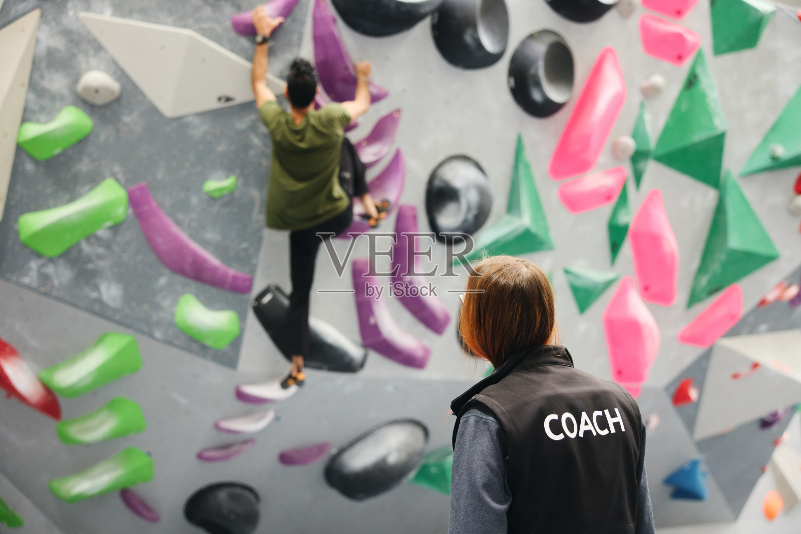 在女教练指导下，男子在室内活动中心攀岩墙照片摄影图片