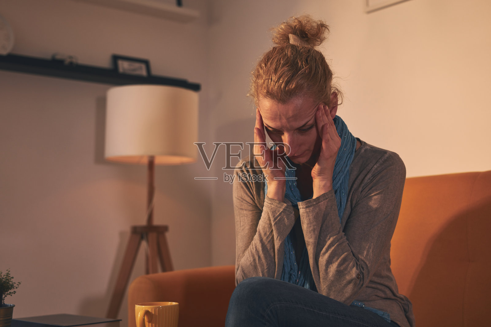 头痛的女人坐在家里的沙发上。照片摄影图片