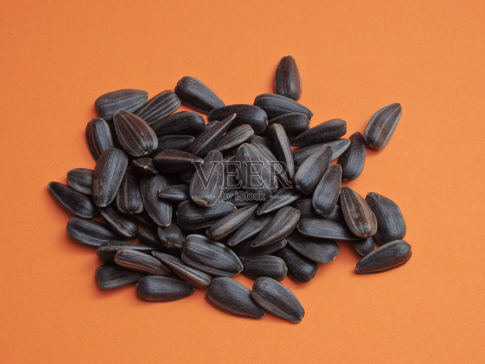 向日葵种子在橙色的背景。美味的向日葵黑色种子的特写，孤立在橙色的背景上照片摄影图片