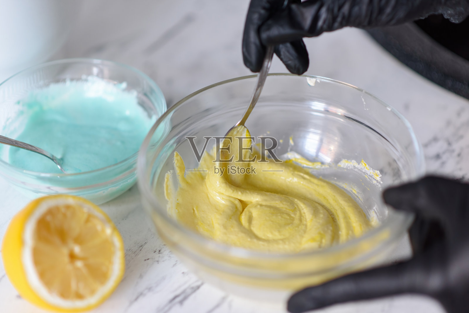 戴着黑色手套的厨师用勺子在玻璃碗里揉面。面包店的概念。照片摄影图片