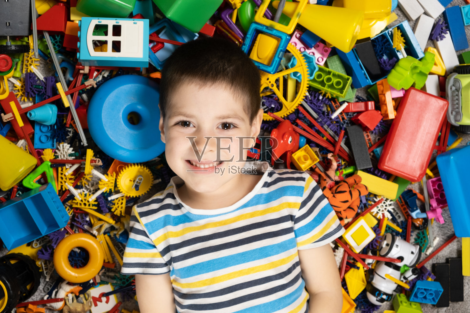 一个5岁男孩的肖像，背景是散落的玩具。童年快乐，玩具丰盈照片摄影图片