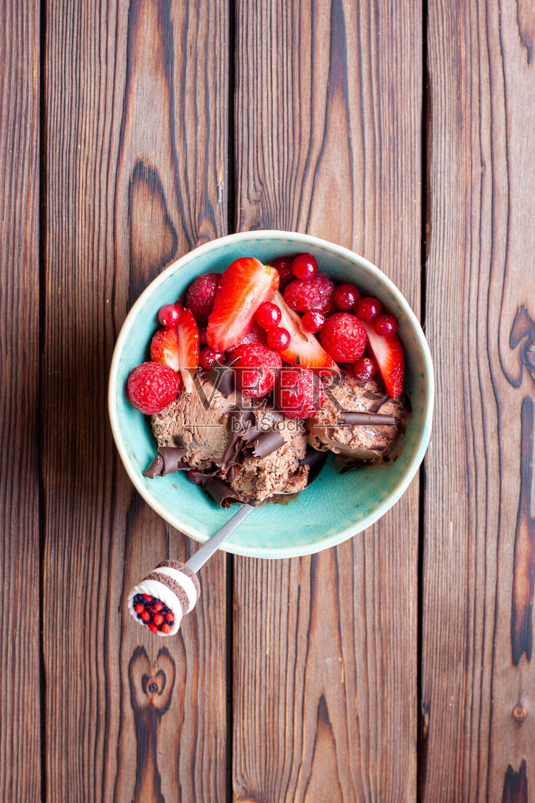 甜的巧克力冰淇淋放在碗里，质朴的木制背景上，配上新鲜的草莓片照片摄影图片