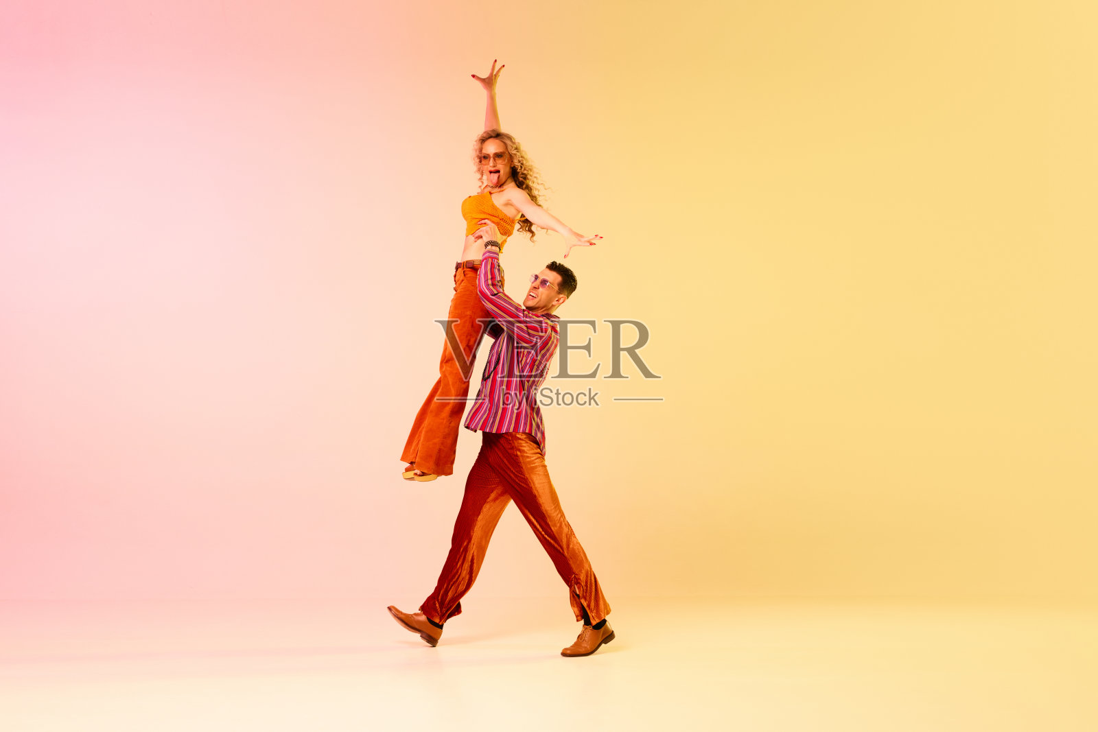的性能。美丽，感性的年轻人，男人和女人穿着复古，时尚的衣服，在渐变的粉黄色背景下跳舞照片摄影图片