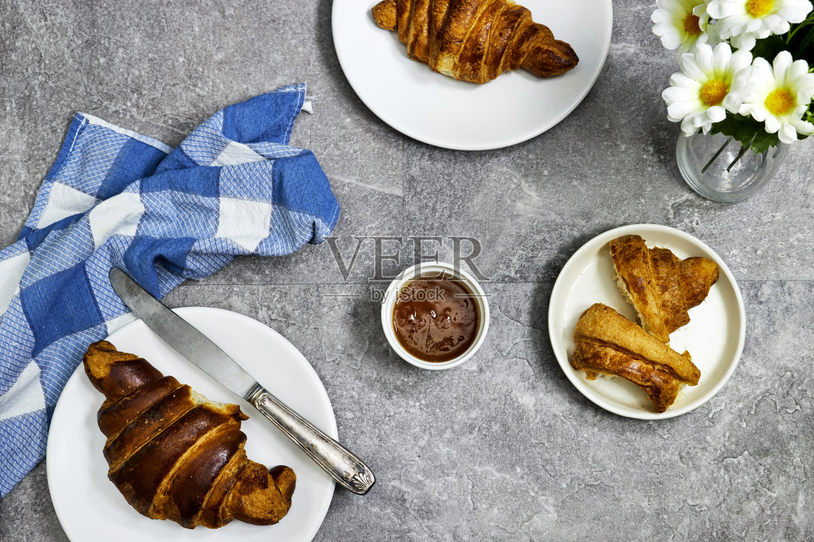 新鲜的甜羊角面包配橙果酱早餐和雏菊花瓶。灰色混凝土桌子上的欧式早餐。前视图。平躺照片摄影图片