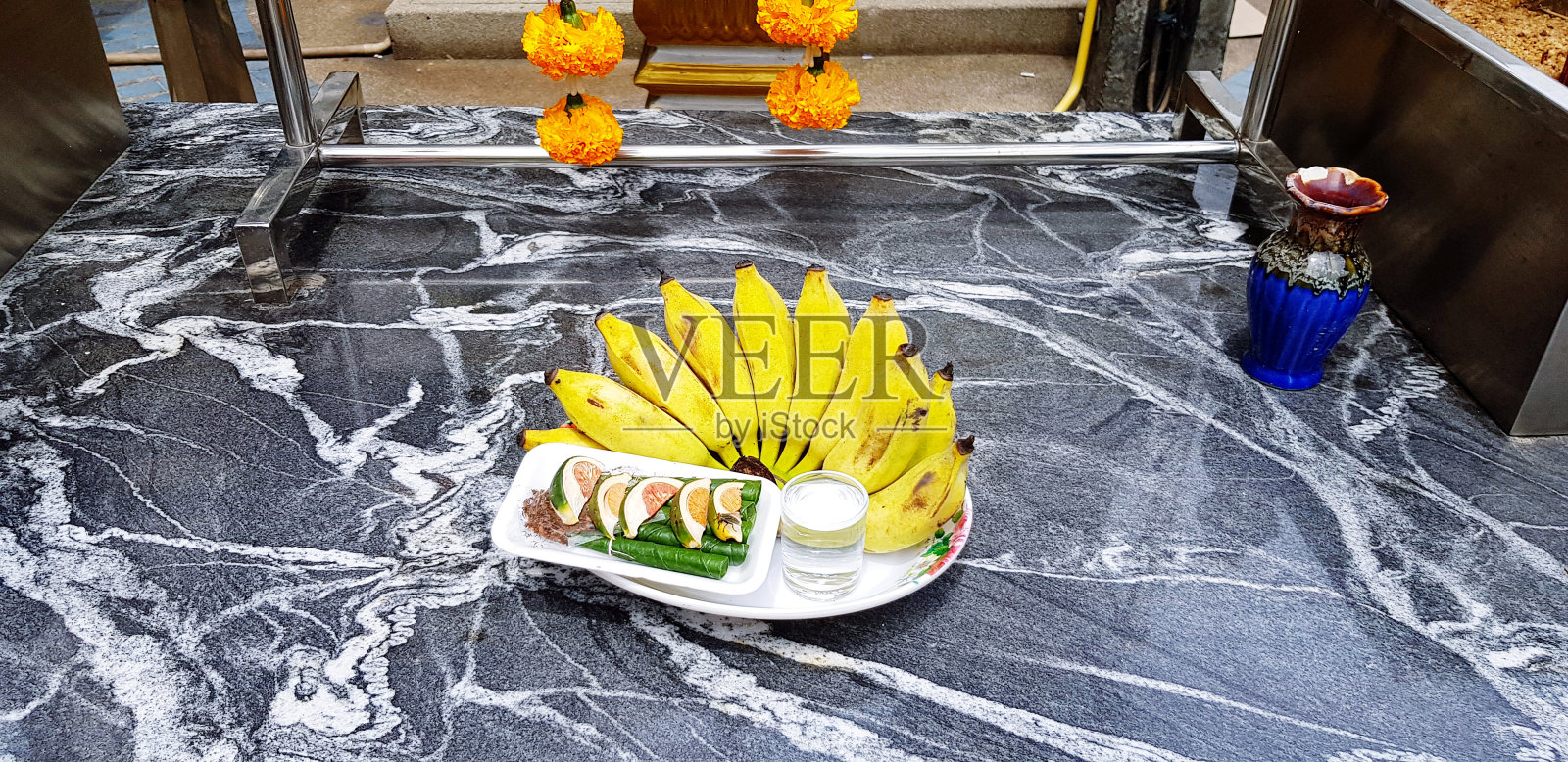 新鲜的香蕉，小杯水和槟榔在白色盘子在黑色大理石桌子上供奉佛像照片摄影图片