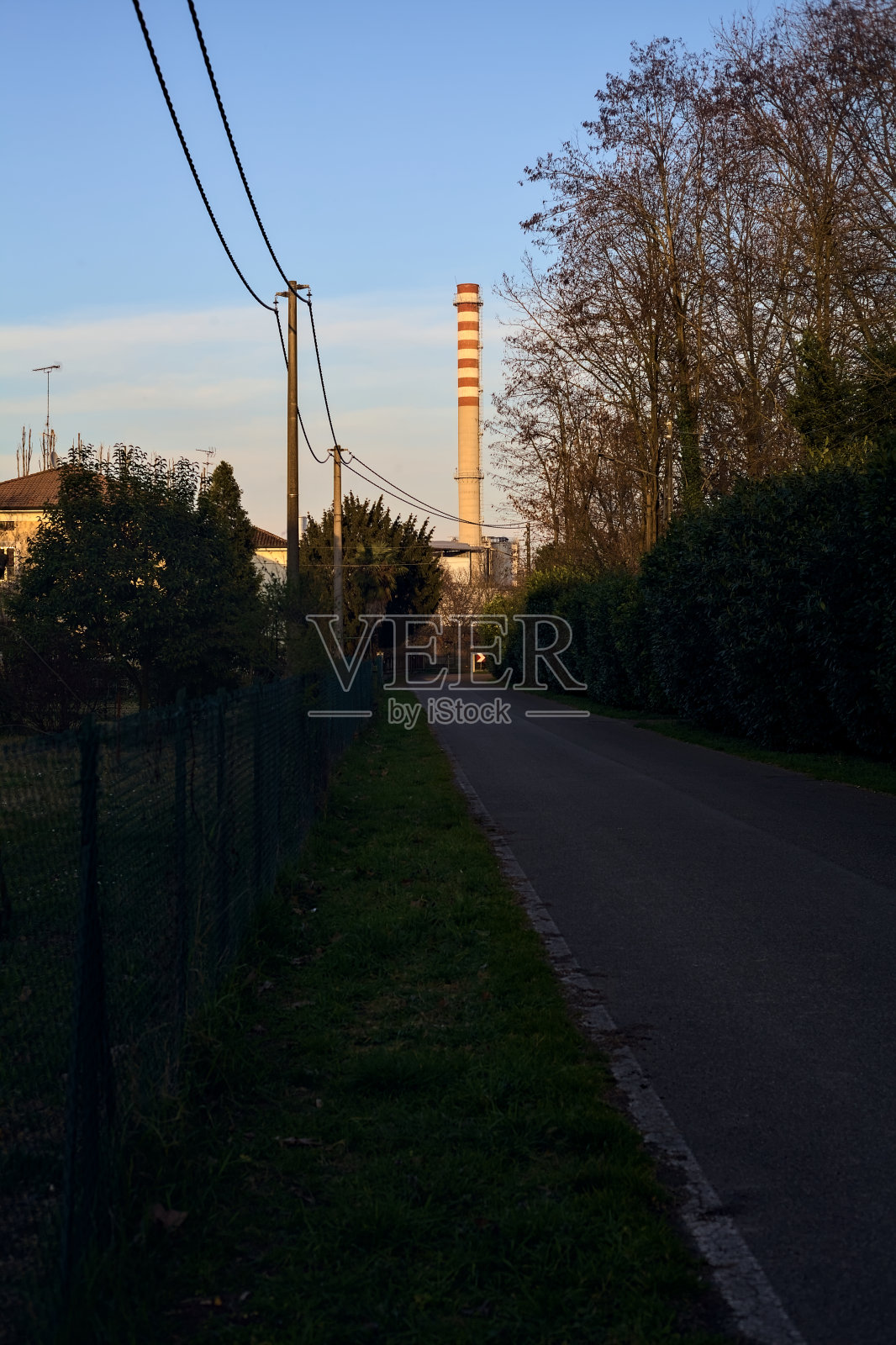 夕阳下的乡间小路上，远处有一个大烟囱照片摄影图片