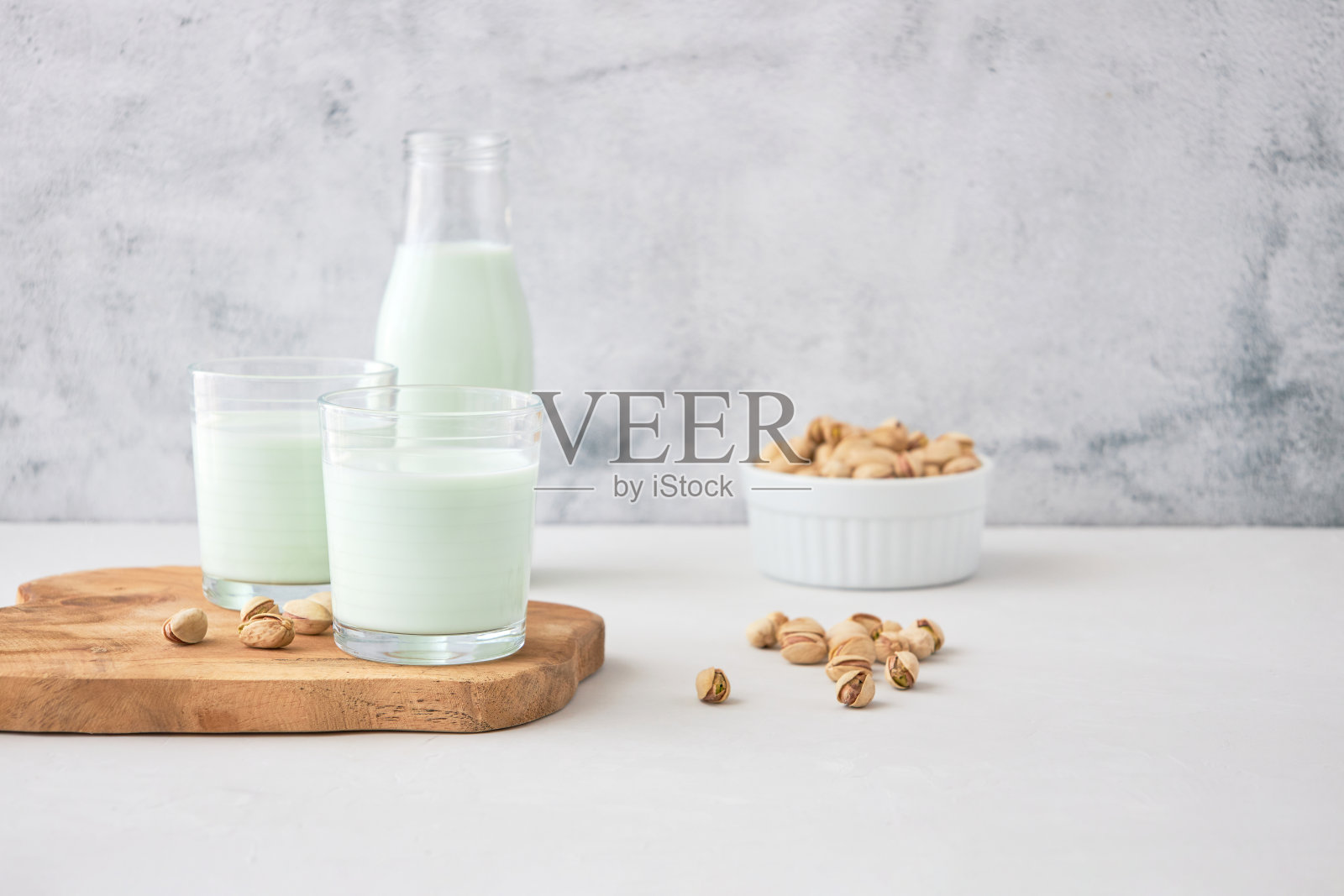 几杯自制的开心果牛奶，放在开心果旁边的木板上。素食者的完美饮品照片摄影图片