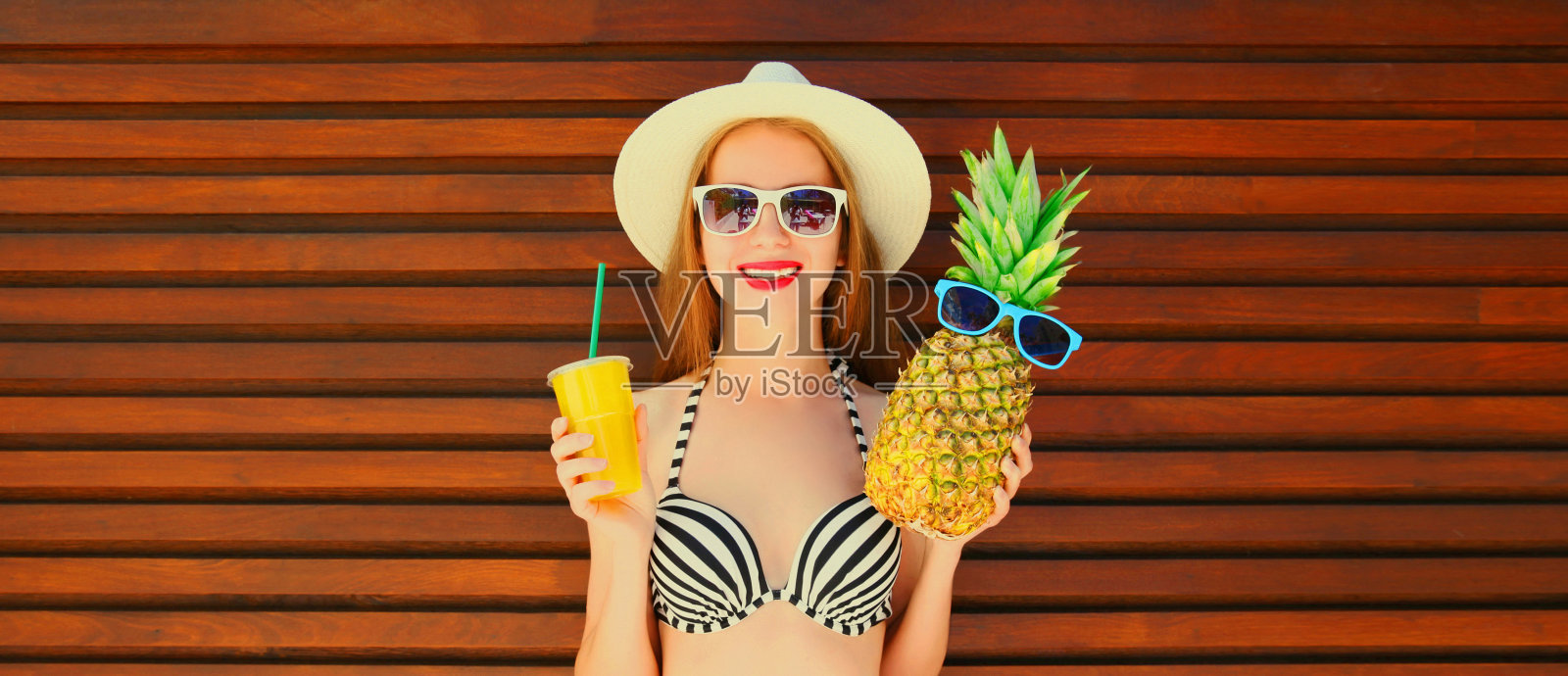夏日肖像的快乐微笑的年轻女子与菠萝和新鲜的果汁杯戴夏季草帽在木制背景照片摄影图片