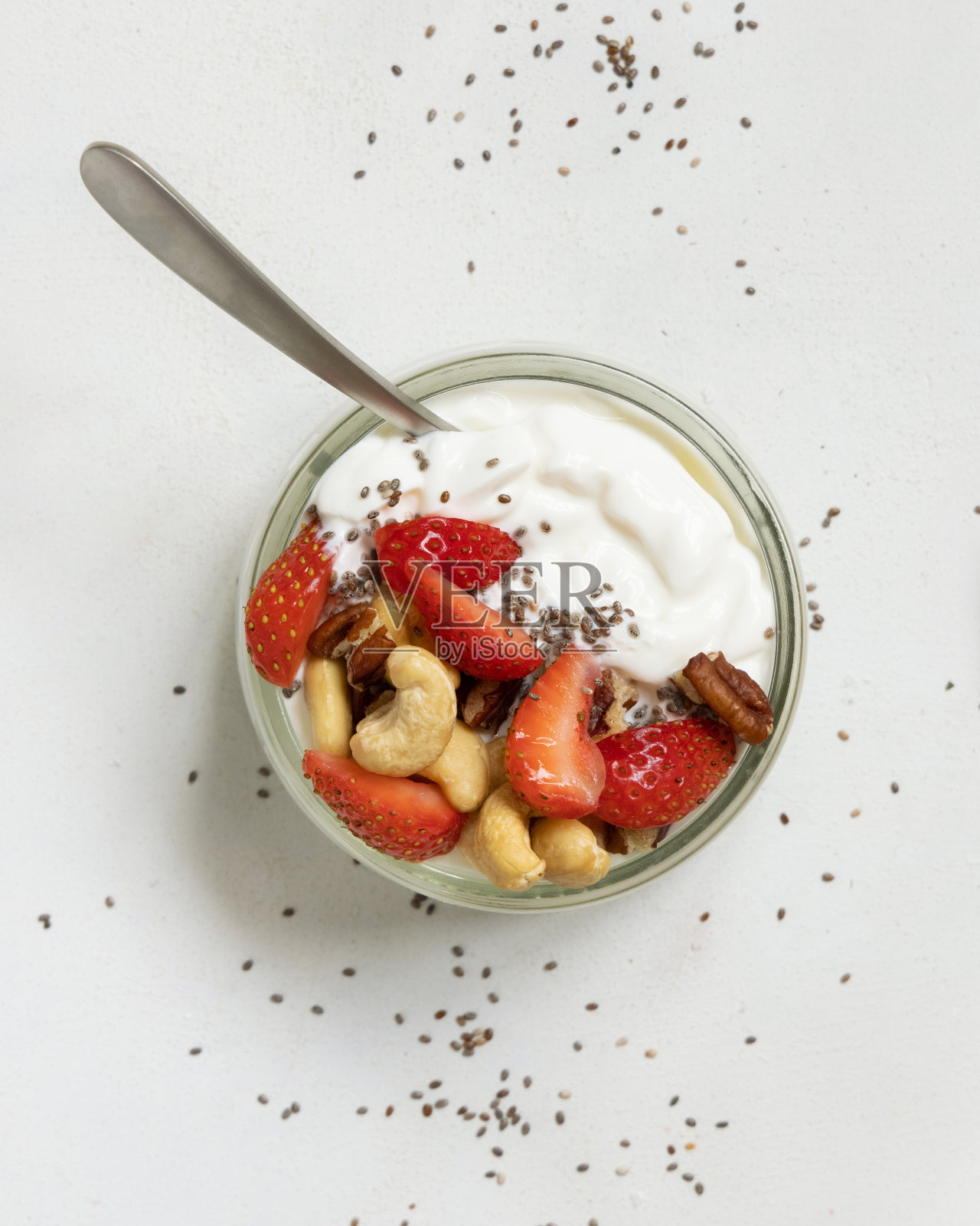 希腊酸奶，坚果和草莓放在一个玻璃罐里，用勺子放在白色的桌面视图上照片摄影图片