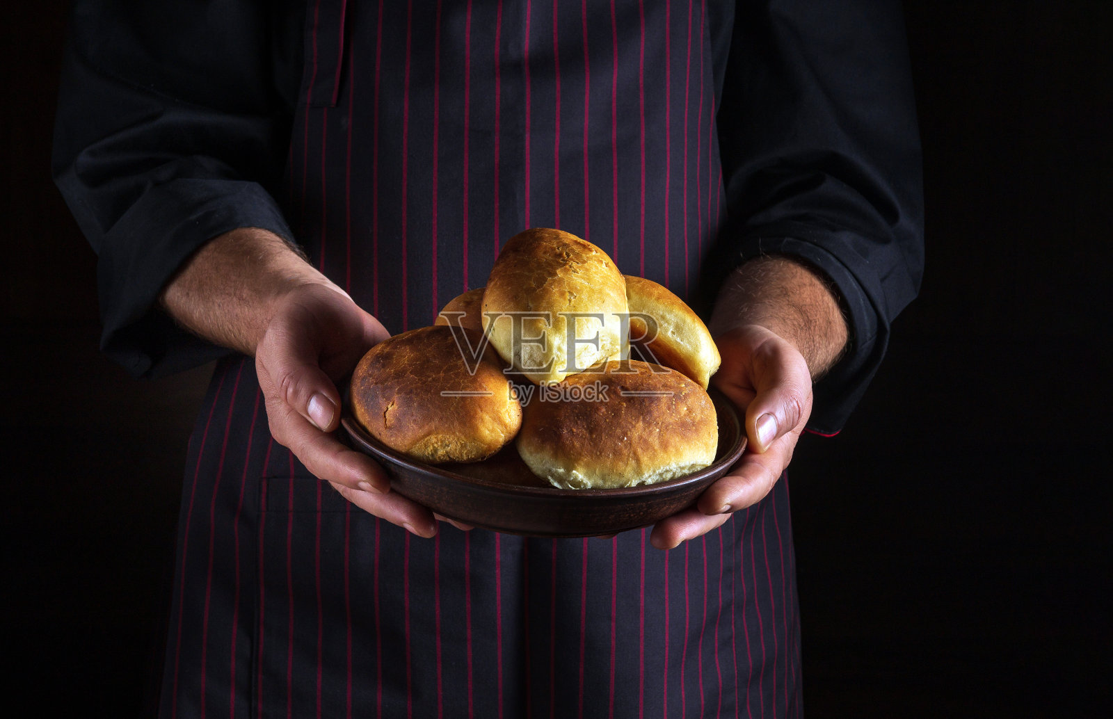 厨师手里拿着一盘刚烤好的馅饼或小圆面包。免费的黑色空间菜单或食谱。照片摄影图片