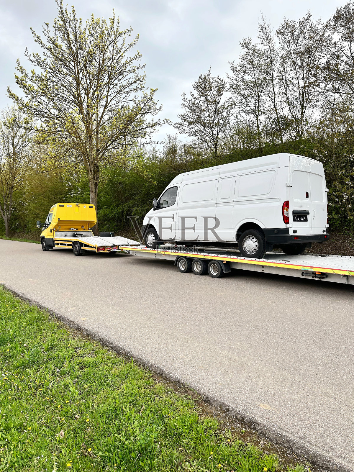 一辆小型卡车用平板拖车在它的背上装载白色的小型货车。汽车服务理念。汽车送货的概念。照片摄影图片