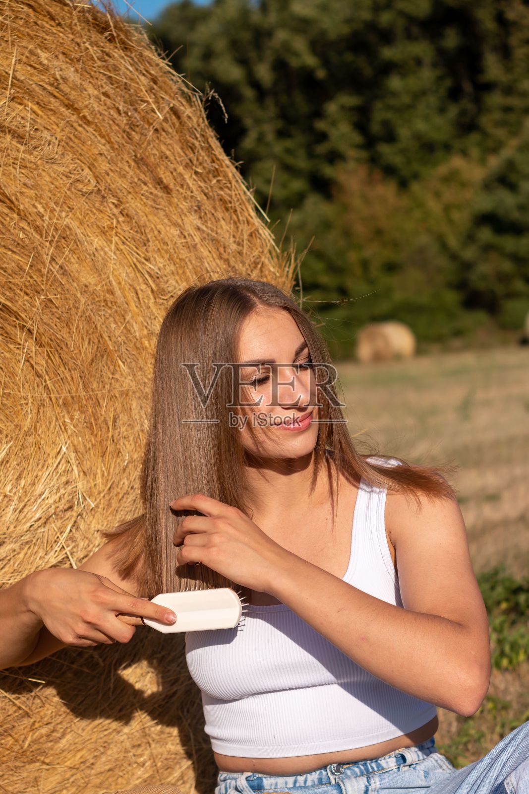 一位年轻的女性站在一堆干草旁，在宁静的乡村环境中梳理着她的长发照片摄影图片