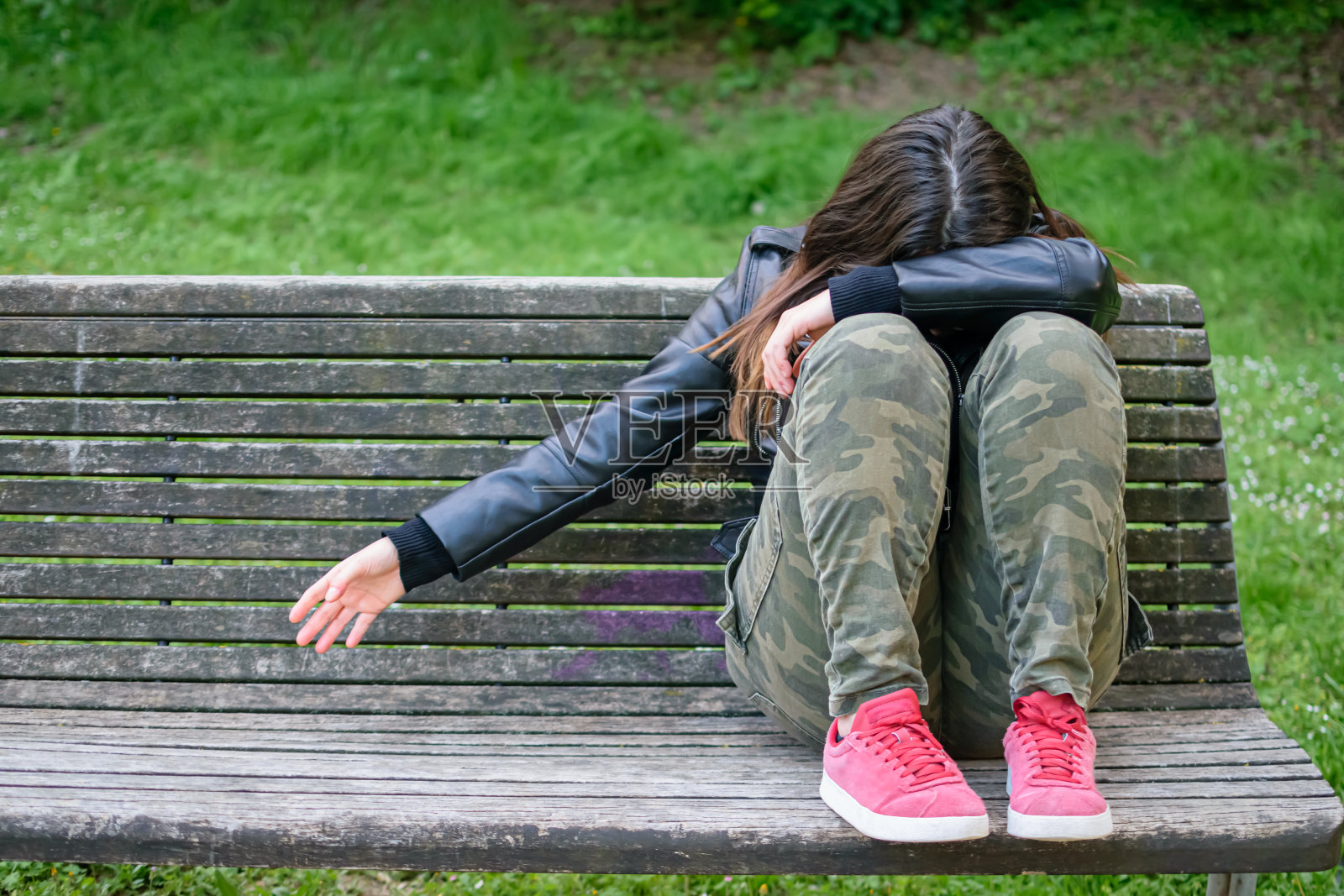 一位年轻女子悲伤而沮丧地坐在公园的长椅上，双臂和头放在膝盖上照片摄影图片