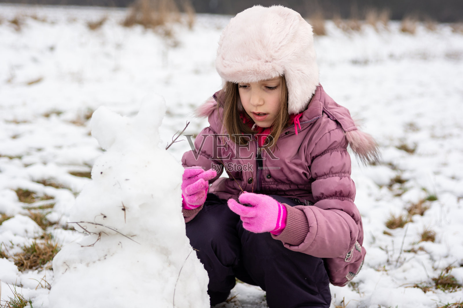 可爱的女孩在冬日草地上堆雪人照片摄影图片