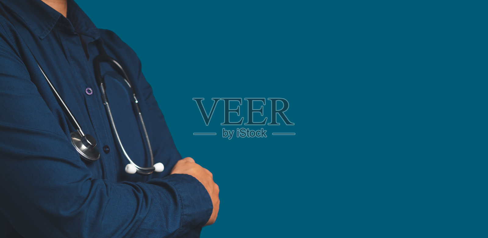 在蓝色背景上，一位医生双臂交叉站立，拿着听诊器照片摄影图片