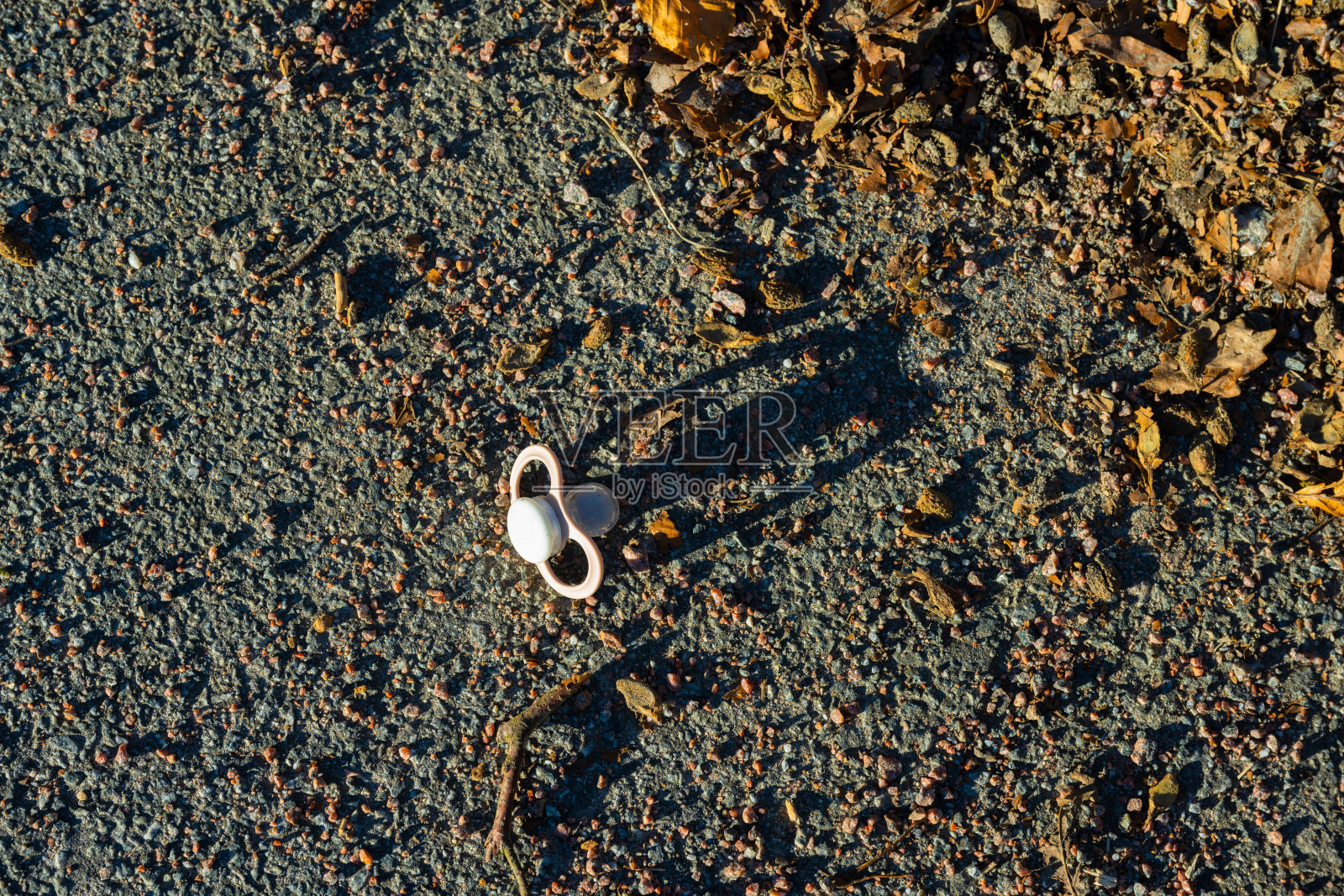 粉红色的奶嘴掉在柏油路和碎石路上。照片摄影图片