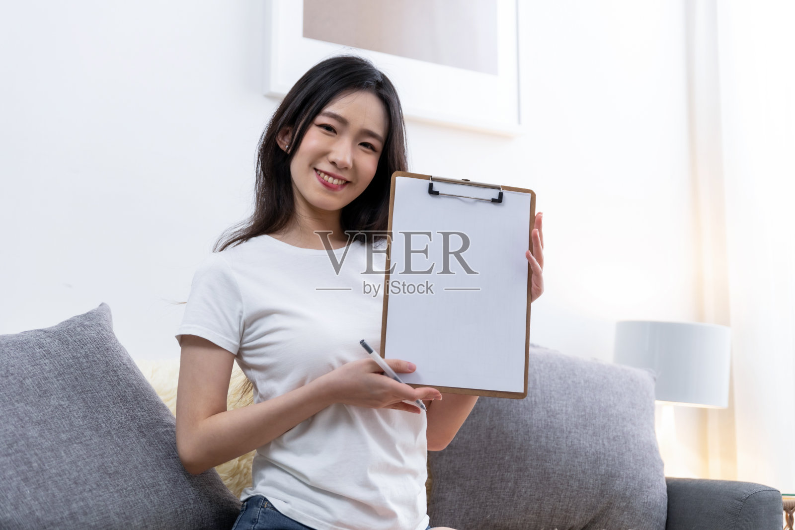 拿着写字板坐在办公室沙发上工作的女性照片摄影图片